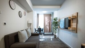 A modern living room with a sofa, a TV mounted on the wall, and a dining area in the background. - Stylish Apartments with Osijek - Standard Studio (Osijek)