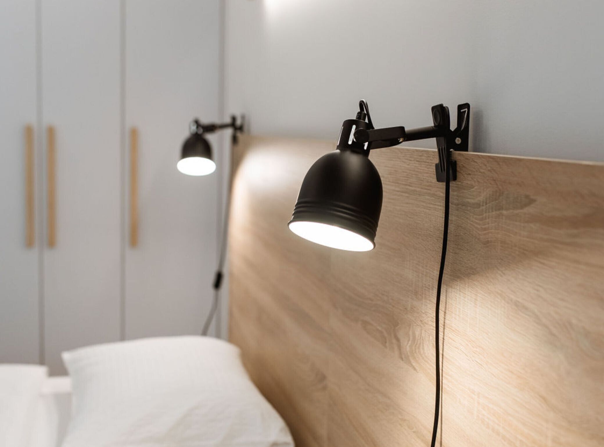 Une chambre à coucher moderne avec une tête de lit en bois, deux lampes de lecture fixées au mur et un lit blanc.