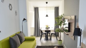 Een moderne woonkamer met een groene bank, een eettafel met stoelen, een potplant en een kleine tafel met een notitieboek en pen.