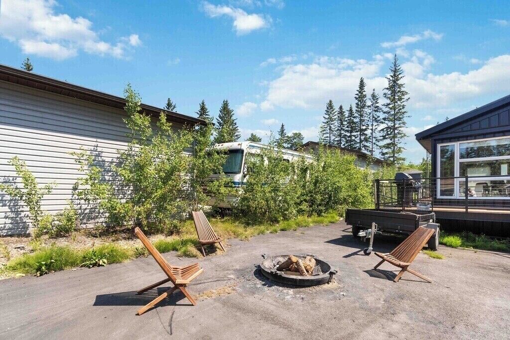 Un terrain de camping équipé d’un foyer, de deux chaises en bois, d’un camion et d’une cabane située dans une zone boisée.