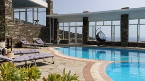 Uma área de piscina com espreguiçadeiras, uma cadeira suspensa e um muro de pedra.
