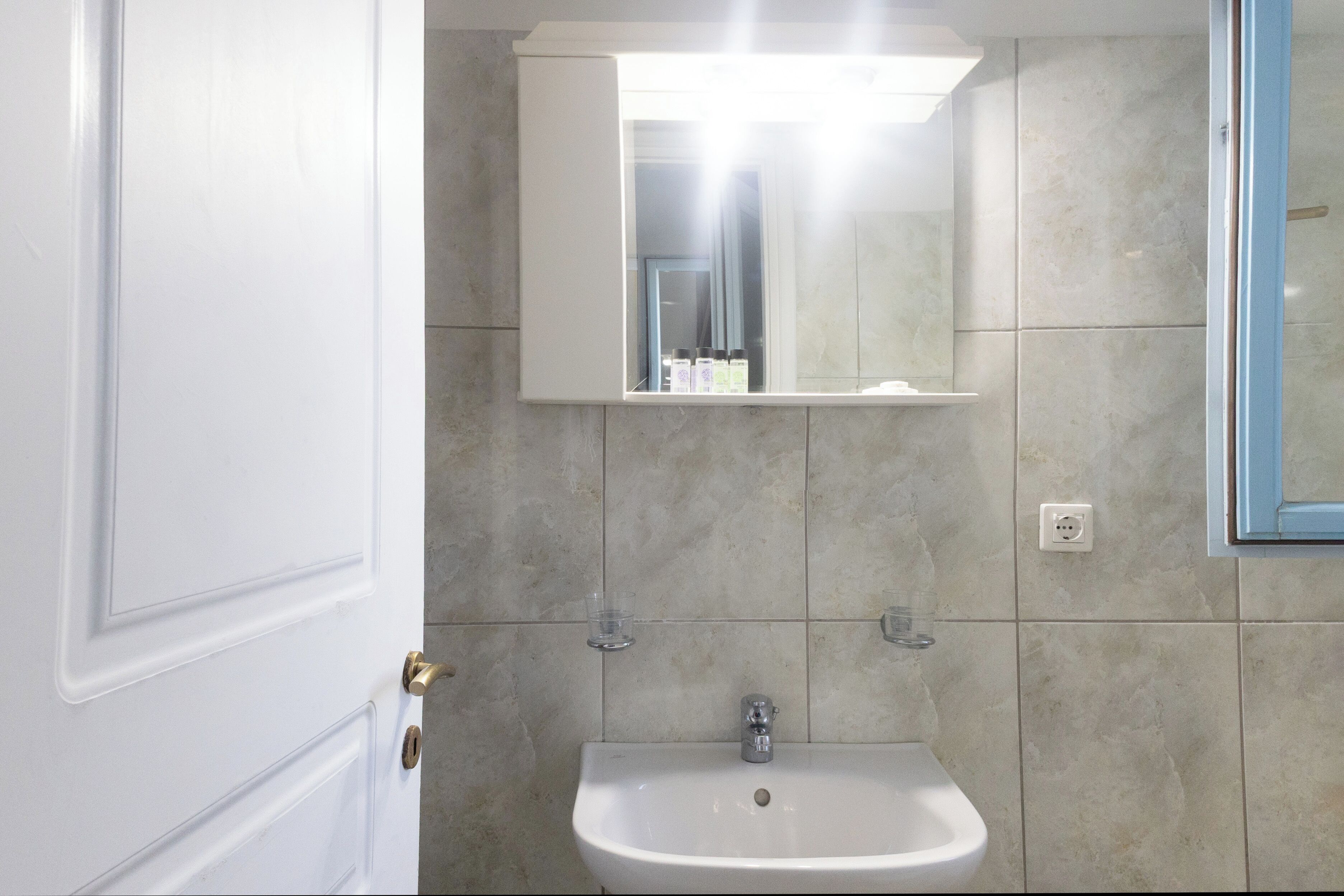 Een badkamer met een witte wasbak, een spiegel erboven en beige betegelde wanden.