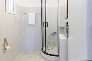 Moderni kylpyhuone, jossa on lasiseinällä varustettu suihku, valkoinen kylpyamme ja wc-paperiteline, jossa on köysi.