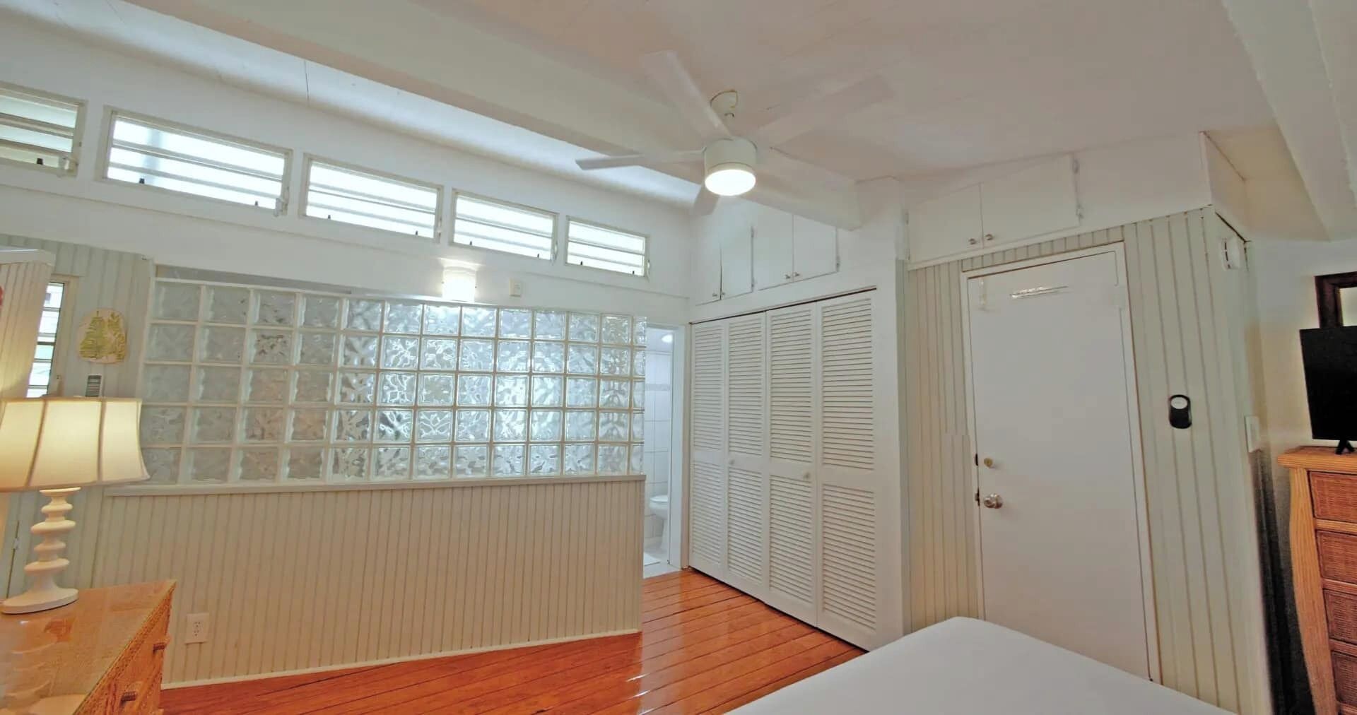 A bedroom with a wooden floor, a window with frosted glass, a ceiling fan, and a wardrobe.
