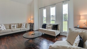 A living room with a beige sofa, a round coffee table, and a view of a green landscape through large windows. - Patio + Pool Table: Lake Marion Getaway (Santee)