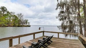 A wooden deck with a table and chairs overlooking a calm lake, surrounded by trees with Spanish moss. - Patio + Pool Table: Lake Marion Getaway (Santee)