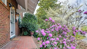 Ein Backsteinhaus mit einer überdachten Veranda, einem Blumentopf und blühenden rosa Blüten.