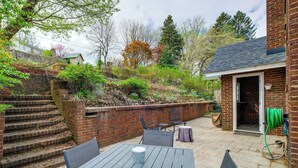 Eine Terrasse mit Tisch und Stühlen, eine Ziegelmauer und ein Garten mit Treppen und Bäumen.