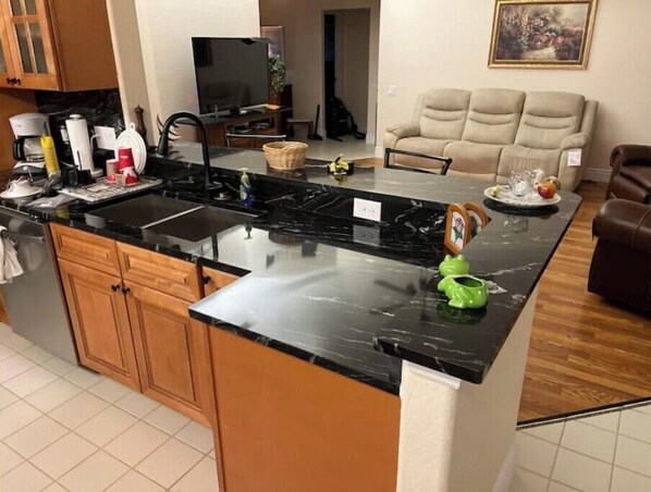 A kitchen with a black countertop, wooden cabinets, and a dining area with a beige sofa.