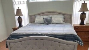 A bedroom with a large bed, two bedside tables, a window with curtains, and a rug on the floor. - Cisky Park Leesburg over looking Lake Harris (Leesburg)