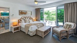 A spacious bedroom with a large bed, a wicker chair, and a view of the outdoors. - Poinciana 012 Hamilton Island & Buggy (Whitsundays)