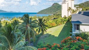 A resort with a view of the ocean, palm trees, and a building with a grey roof. - Poinciana 012 Hamilton Island & Buggy (Whitsundays)
