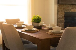 Una mesa de comedor con cuencos y platos blancos, una planta en maceta y una chimenea de piedra.