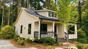 A single-story house with a porch, surrounded by trees and a gravel driveway. - Cedar Creek Cottage 5 minutes to town! (Cashiers)