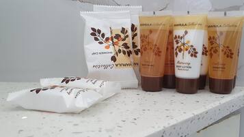 Un meuble-vasque de salle de bain avec un lavabo en marbre blanc, une serviette blanche et quatre flacons de lotion corporelle et de shampoing de la collection Marula.