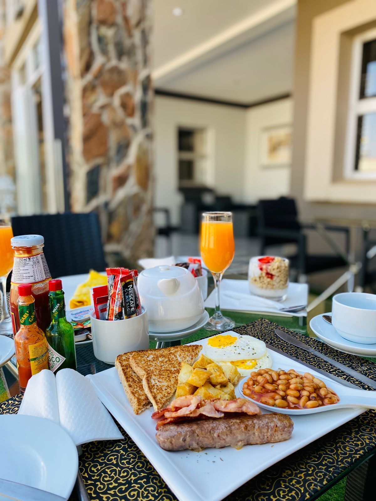A breakfast table with toast, eggs, beans, sausage, and juice.