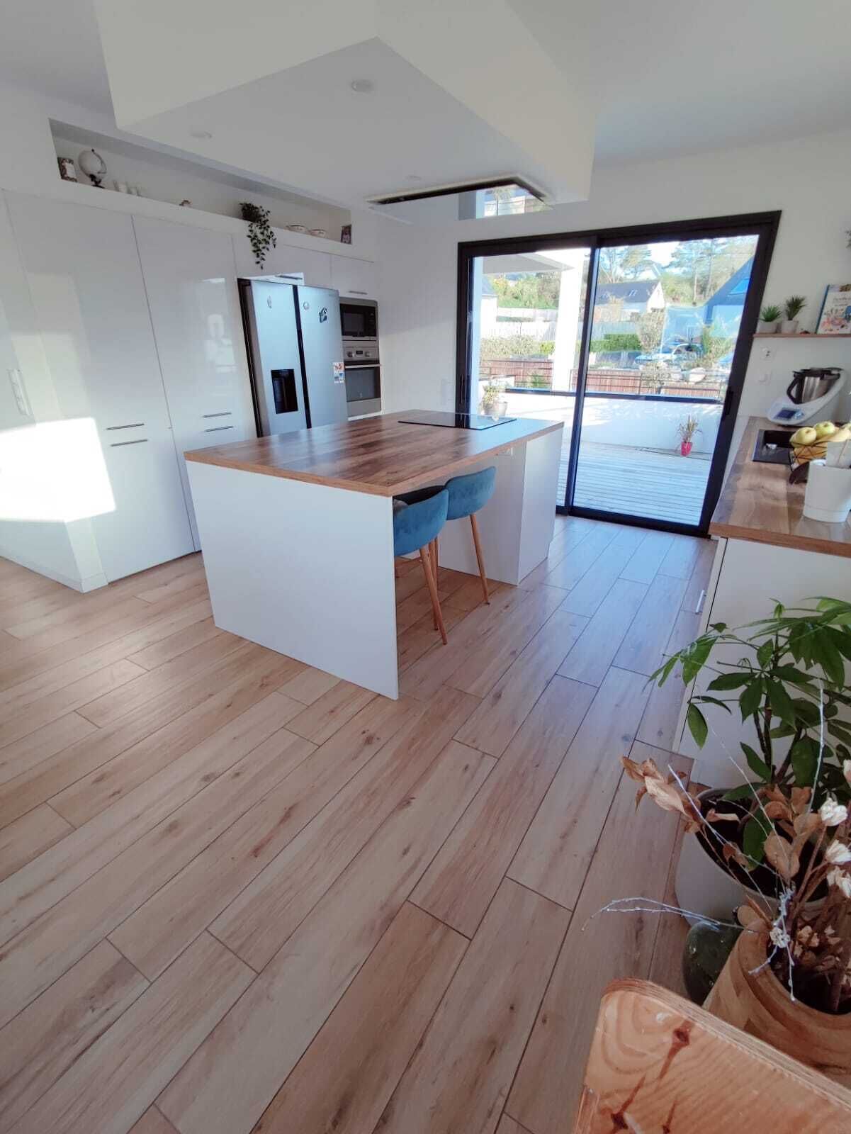 Uma cozinha moderna com armários brancos, uma ilha de madeira e uma porta de vidro deslizante que dá para uma varanda.