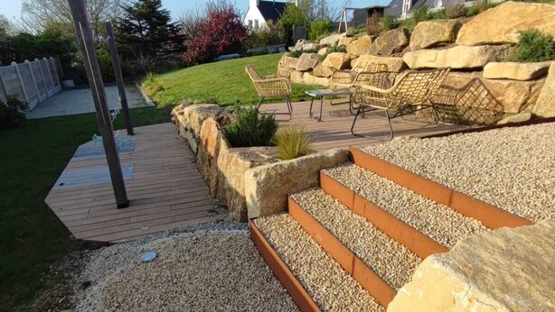Un jardín con terraza de madera, macetas de piedra y mobiliario exterior.