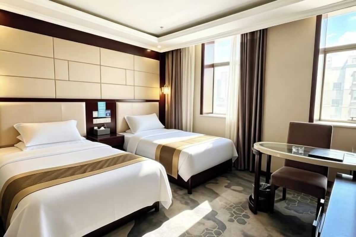 A hotel room with two beds, a desk, and a chair.