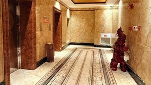 A marble-floored hallway with a patterned carpet, a wooden door, and a red decorative statue. - Jinrun Holiday Hotel (Korla)