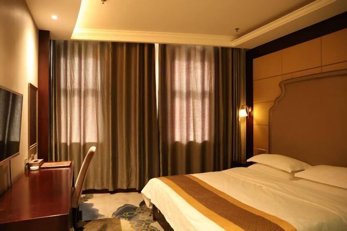 A hotel room with a bed, a TV, a desk, and curtains.