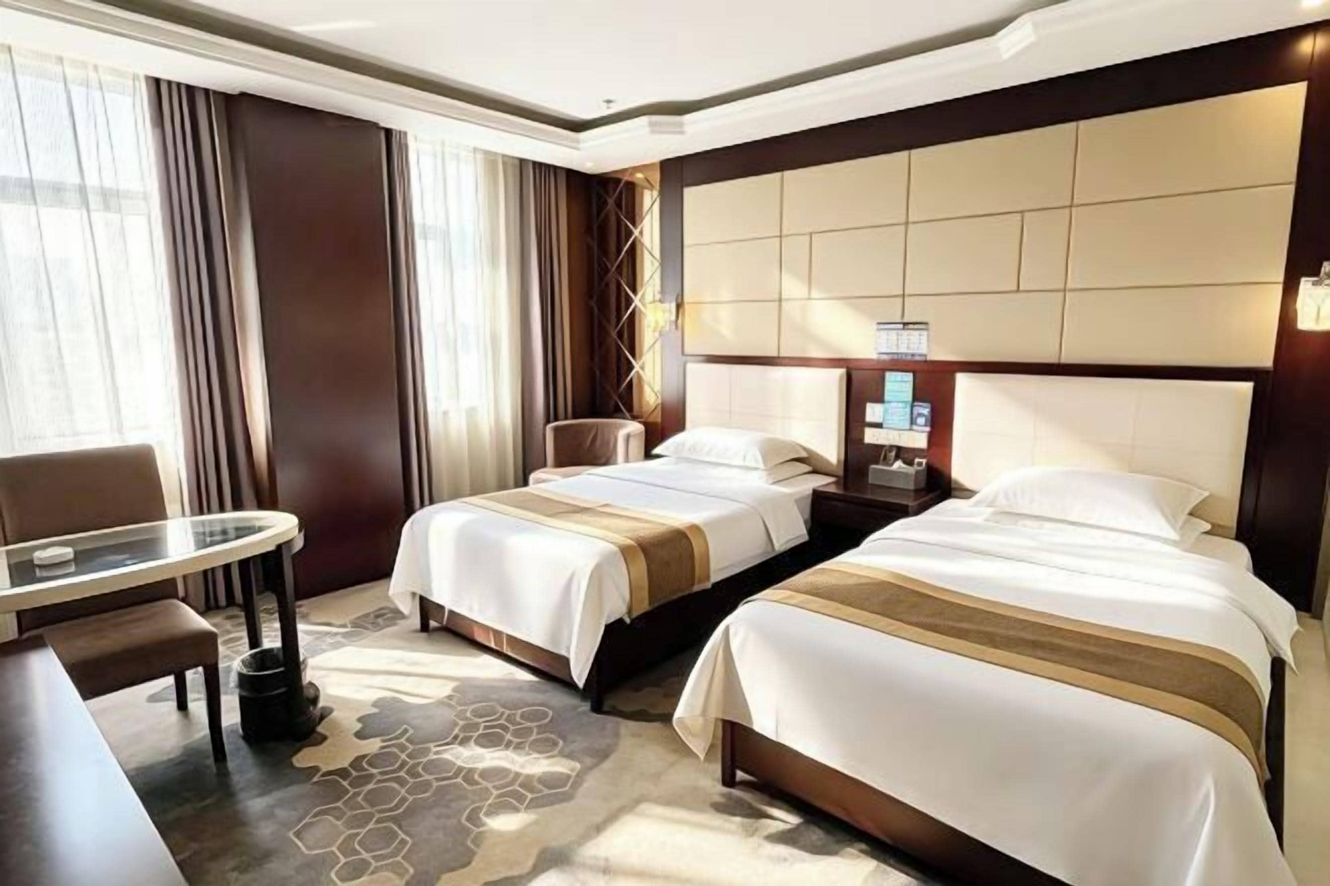 A hotel room with two beds, a desk, a chair, and a large window with curtains.