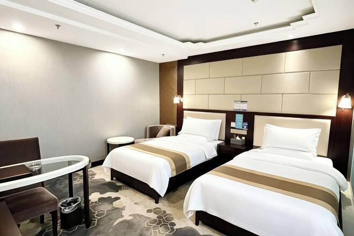 A hotel room with two beds, a small table, a chair, and a nightstand with a lamp.