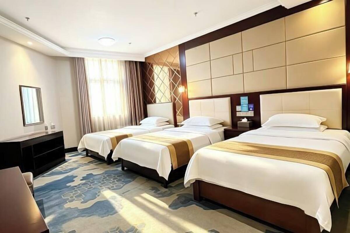 A hotel room with two beds, a desk, a chair, a TV, and a large window with curtains.