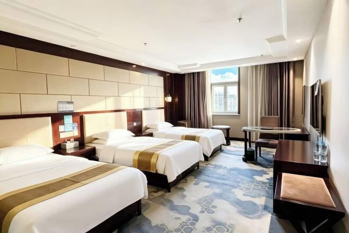 A hotel room with two beds, a desk, a chair, a small table, a TV, and a window with curtains.