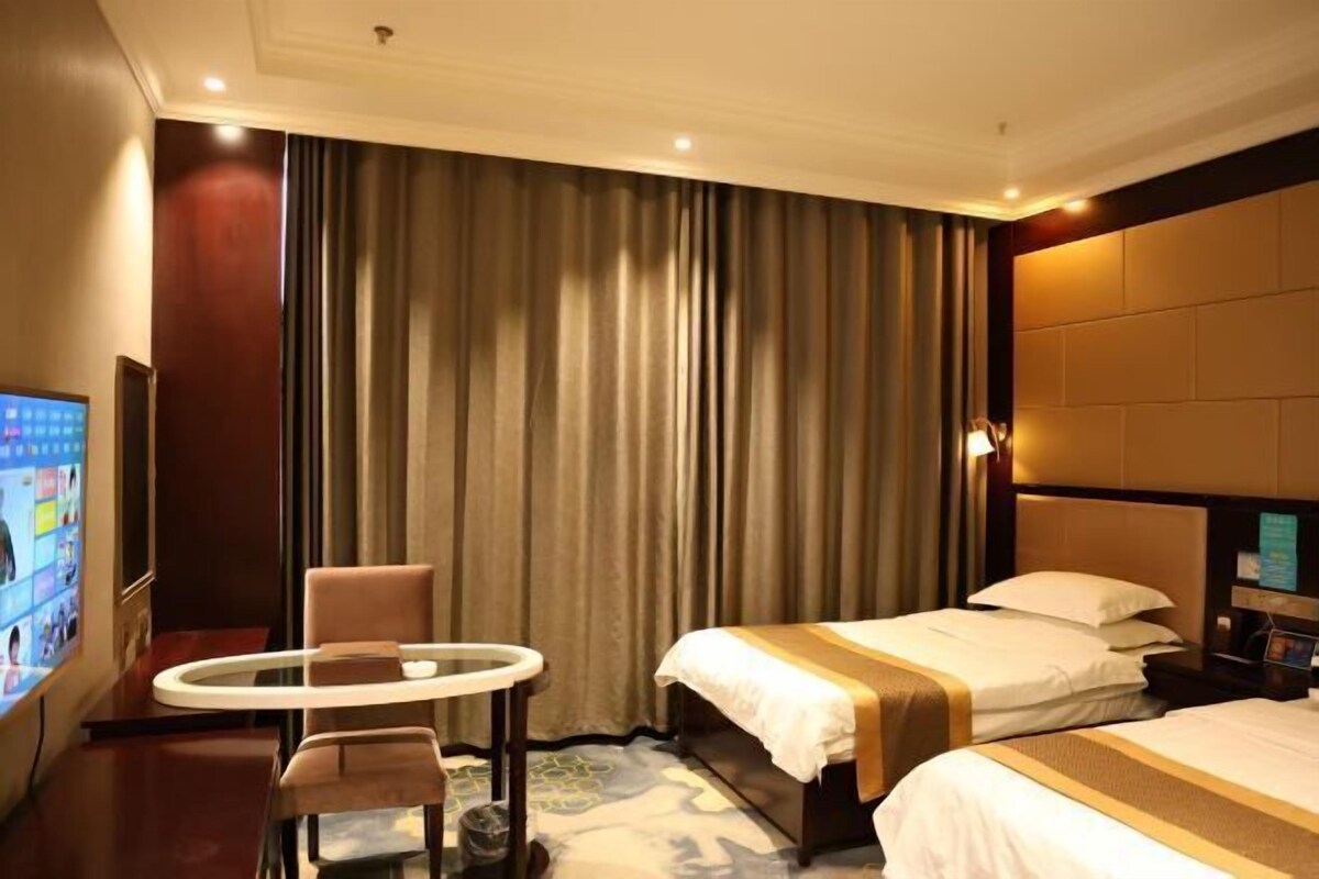 A hotel room with a bed, a small round table, a chair, a TV, and a curtain.