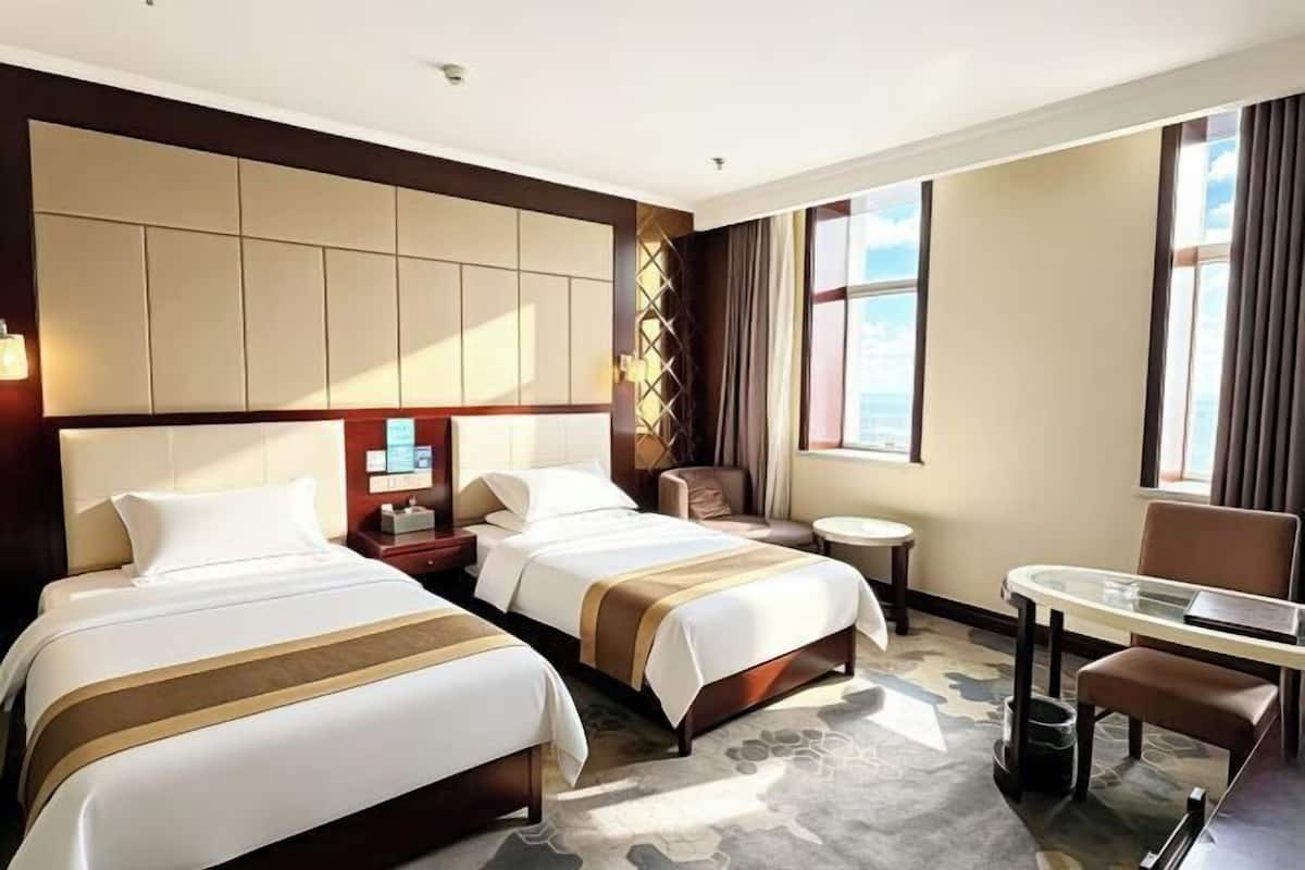 A hotel room with two beds, a desk, a chair, a small table, and a window.