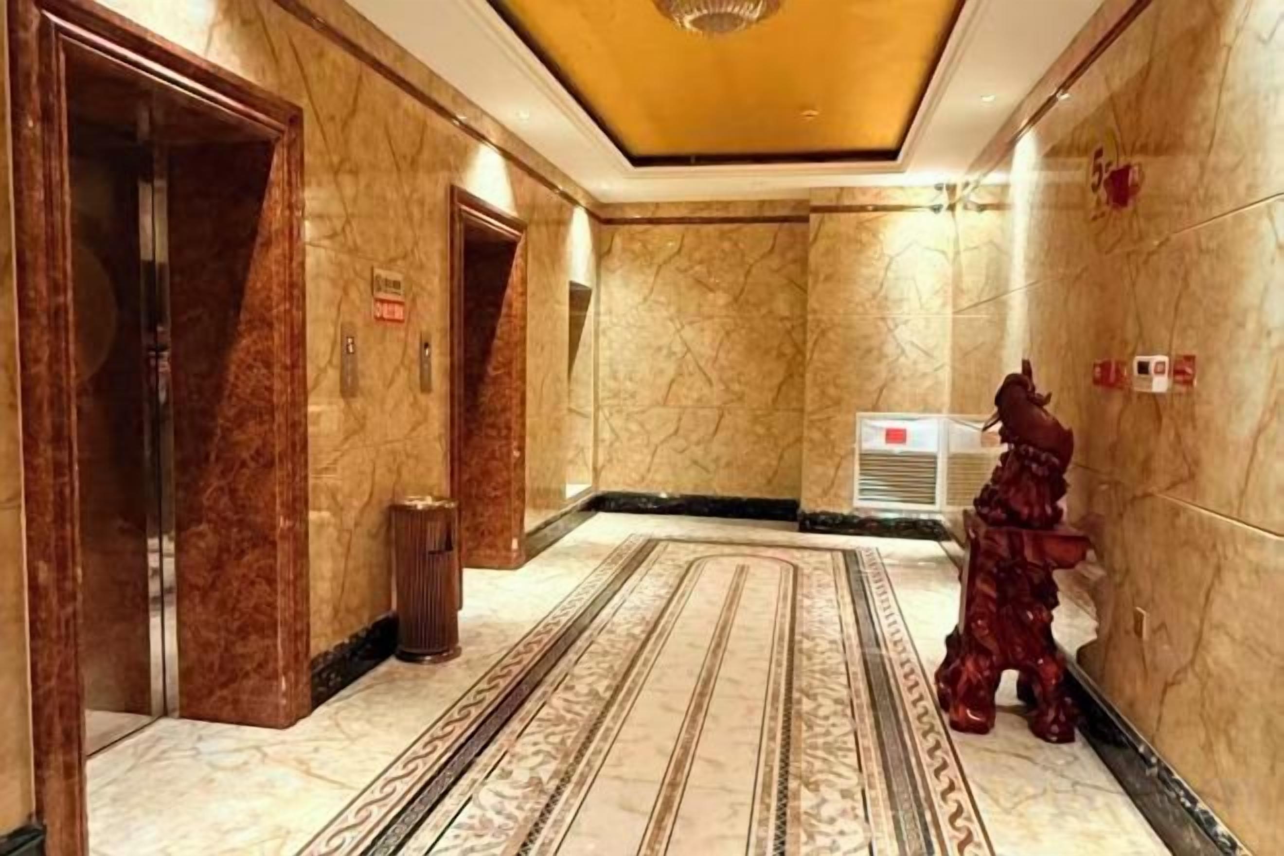 Pasillo de hotel con paredes de mármol, alfombra estampada y una estatua.