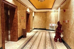 A hotel corridor with marble walls, a patterned carpet, and a statue. - Jinrun Holiday Hotel (Korla)