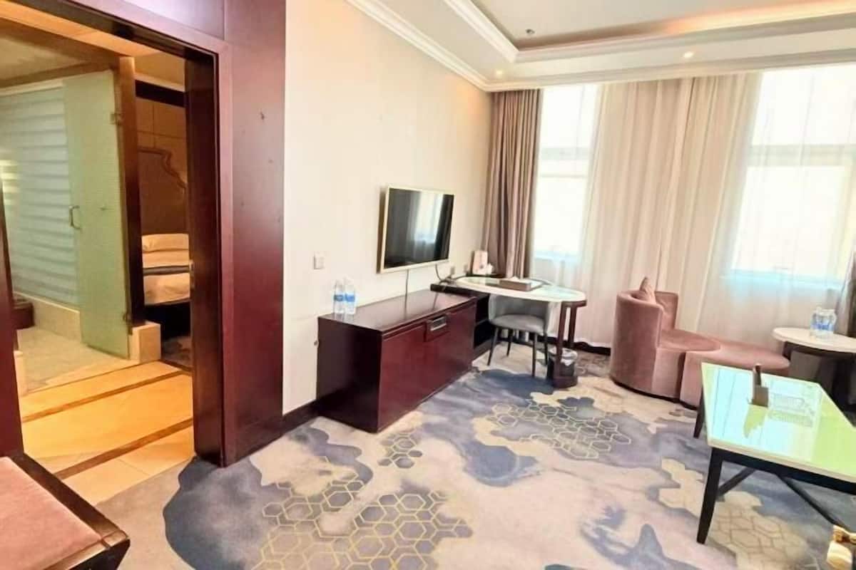 A hotel room with a bed, a desk, a television, a chair, a small table, and a window with curtains.