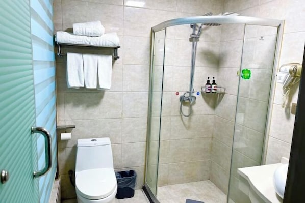 A bathroom with a glass-enclosed shower, a toilet, a sink, and a towel rack with towels. - Jinrun Holiday Hotel (Korla)
