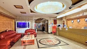 A lobby with a reception desk, a red sofa, a coffee table, and a patterned floor. - Jinrun Holiday Hotel (Korla)