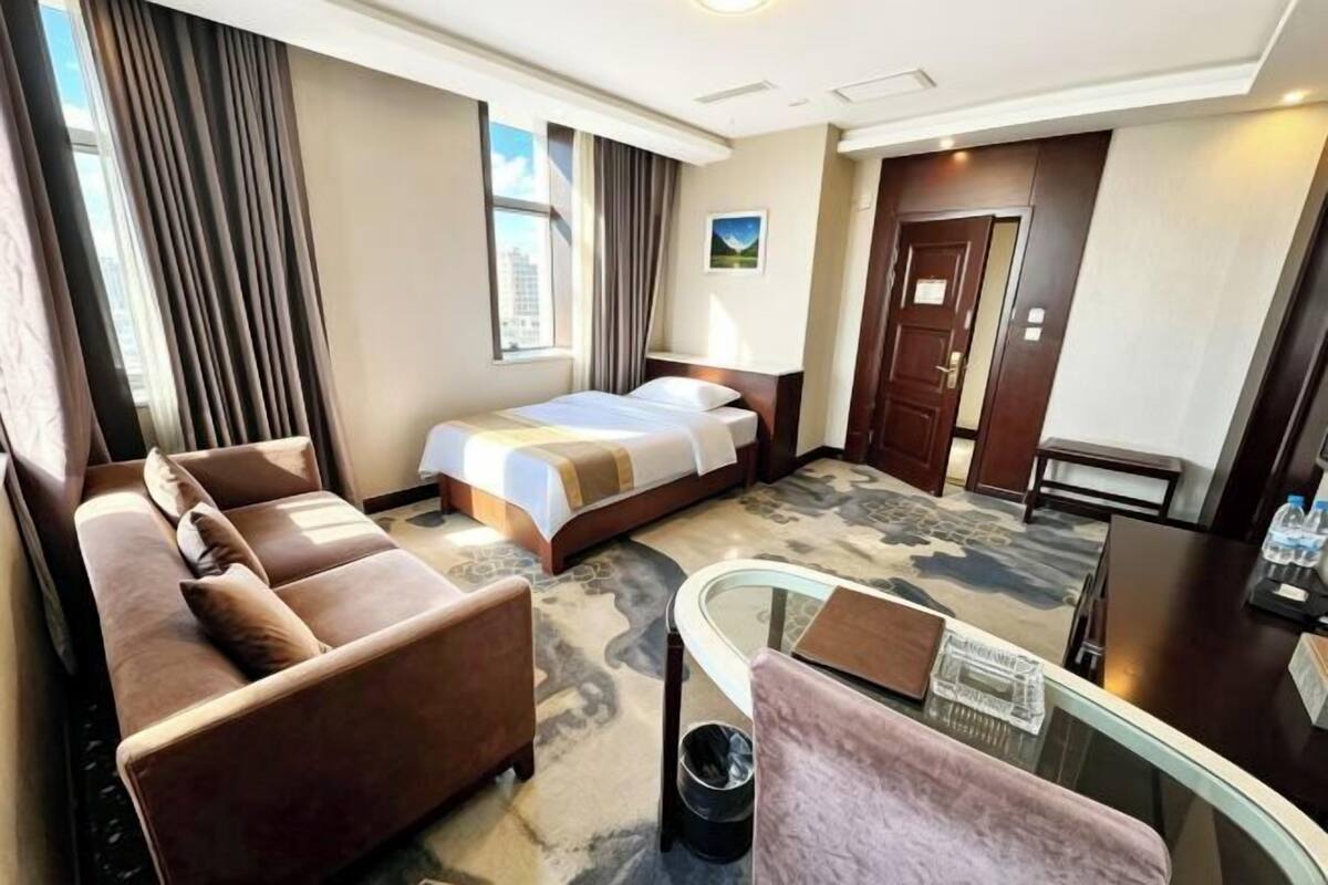 A hotel room with a bed, sofa, glass table, and a view of the city.