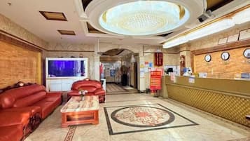 A hotel lobby with a reception desk, a large television, leather sofas, and a patterned carpet.