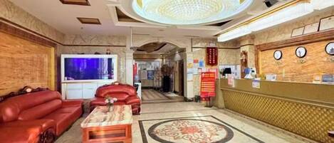 Un vestíbulo de hotel con una recepción, un televisor grande, sofás de cuero y una alfombra estampada.
