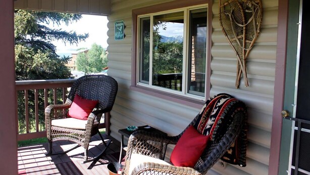A porch with wicker chairs, a small table, and a view of trees and mountains. - View of Lake Granby - LOCATION (Grand Lake)