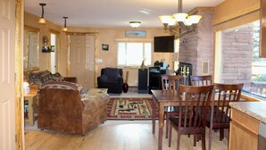 A cozy living room with a fireplace, a dining area with wooden chairs, and a kitchen with a brick wall. - View of Lake Granby - LOCATION (Grand Lake)
