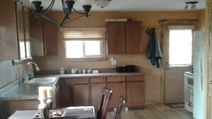 A kitchen with wooden cabinets, a dining table with chairs, and a window with blinds. - View of Lake Granby - LOCATION (Grand Lake)