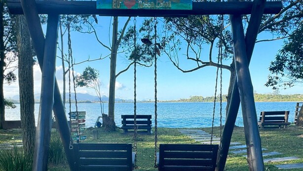 A swing set with benches, a clear view of a lake, and a signboard with directions. - Casa Aconchegante na Lagoa de Ibiraquera (Imbituba)