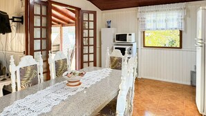 A dining area with a long table, white chairs, a lace table runner, and a view of the outdoors through a window. - Casa Aconchegante na Lagoa de Ibiraquera (Imbituba)