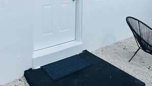 A white house with a number 5 door, a window, and a black chair outside. - Wilton Manors Guesthouse #5 (Wilton Manors)