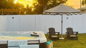 A backyard with a hot tub, two Adirondack chairs, a striped umbrella, and a white picket fence. - Wilton Manors Guesthouse #5 (Wilton Manors)
