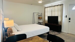 A hotel room with a bed, a TV, a lamp, a shelf with towels, and a door. - Wilton Manors Guesthouse #5 (Wilton Manors)