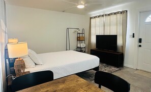 Une chambre d’hôtel avec un lit, une télévision, une lampe, une étagère avec des serviettes et une porte.