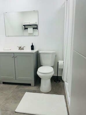 Een badkamer met een wit toilet, een grijs kastje, een spiegel en een witte kleed.