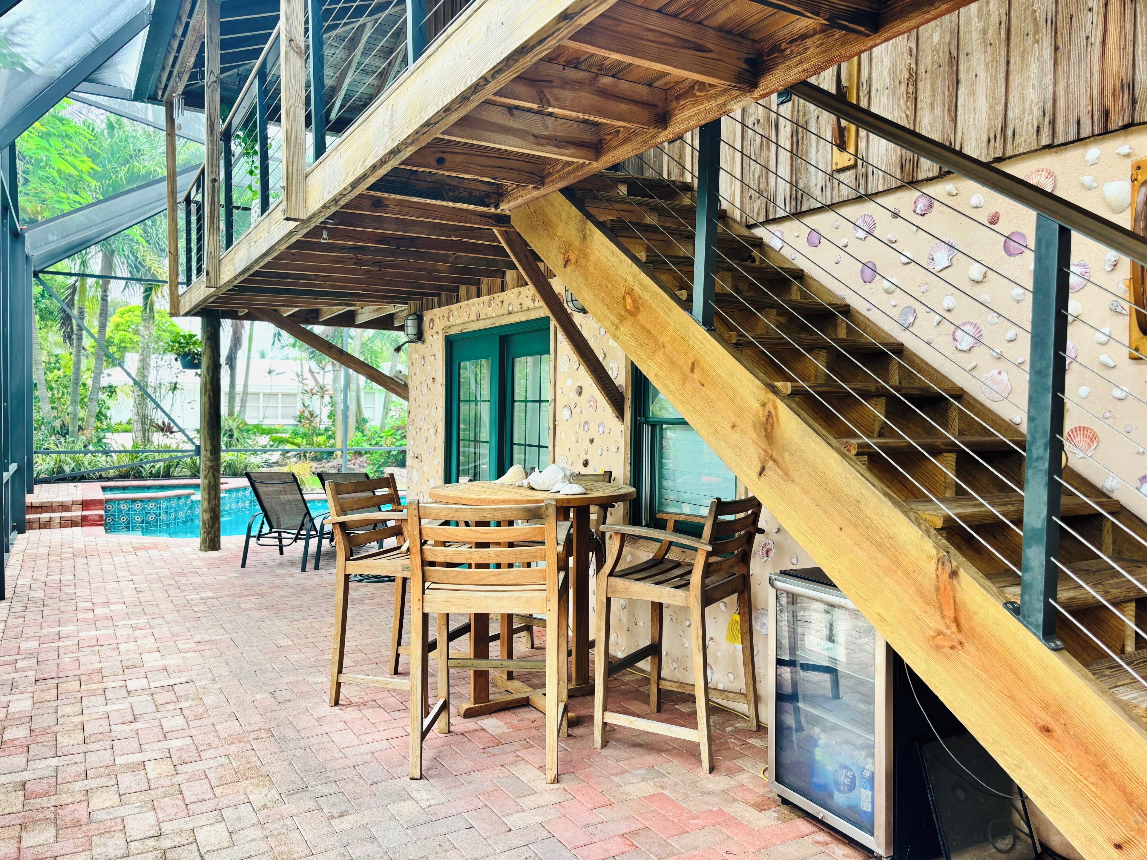 A wooden staircase with a railing, a pool, and outdoor seating with chairs and a table.